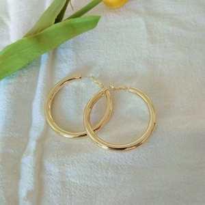 Close-up of polished gold hoop earrings on soft white linen with green floral accents