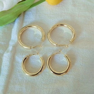 Close-up of small and large polished gold hoop earrings on a textured fabric background