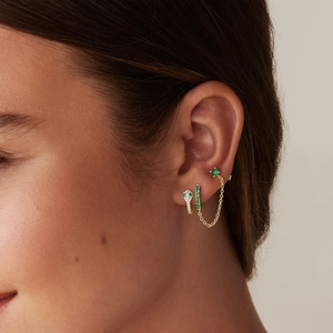 Detail of gold snake earrings with green gemstones and zircon stones on a model