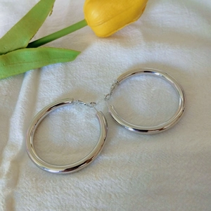 Detailed view of large silver-tone hoop earrings on white fabric with a yellow tulip