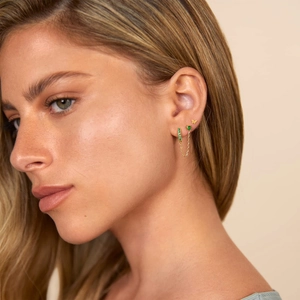 Macro detail of 14K gold butterfly studs and green gemstone chain earrings on ear