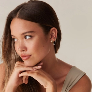 Detailed view of layered gold ear piercings with green zircon and a delicate nose ring