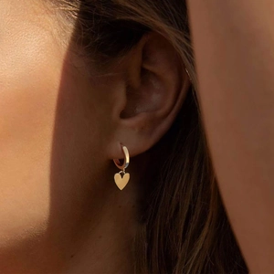 Detail of a minimalist gold heart pendant earring worn for a stylish fashion look