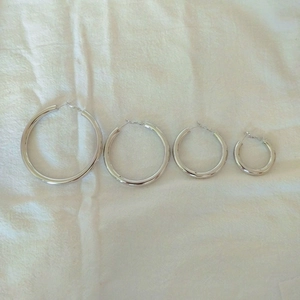 Detailed comparison of four polished silver hoop earrings in varying sizes on white fabric