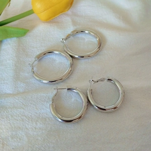 Two pairs of polished silver hoop earrings on a minimalist white linen background