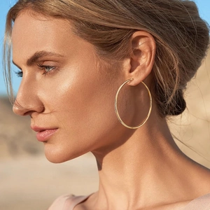 Close-up of a model wearing large gold hoop earrings with a high-shine polished finish