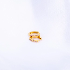 Macro view of gold hoop earrings with pink cubic zirconia on white silk background