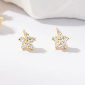 Gold star stud earrings with pave zircon stones on a white stone background