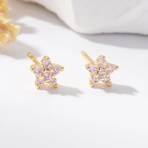 Macro shot of gold star stud earrings with pink cubic zirconia on a stone surface