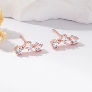 Detail showing curved rose gold earrings with three round cubic zirconia on a white surface