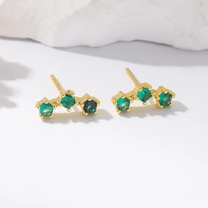 Elegant gold earrings with three green cubic zirconia stones on white stone pedestal