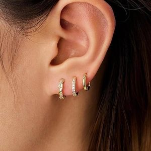 Close-up of a model wearing three different gold plated huggie earrings set with zircons