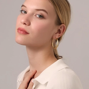 Detailed close-up of chunky gold-tone twisted hoop earrings worn by a model