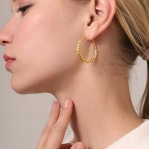 Close-up of gold braided hoop earrings showing fine twisted metal texture on female model