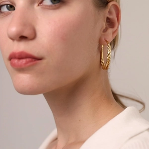 Close-up of model wearing chunky twisted golden hoop earrings with woven texture detail