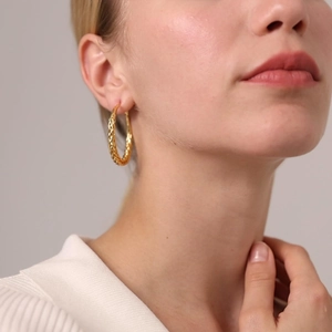 Macro view of gold braided chunky hoop earring featuring a woven texture on model