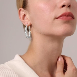 Close-up of a silver braided hoop earring worn by a model with delicate woven textures
