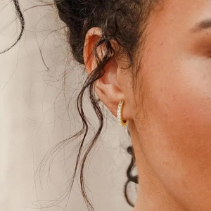 Close-up of elegant gold U-shaped huggie earrings with cubic zirconia on a model