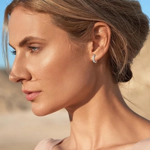 Close-up of sparkling 14K gold C-shaped earrings with rhinestones on a female model