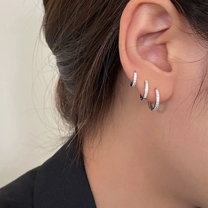 Detalle de tres pendientes huggie de plata de ley con circonitas puestos en la modelo