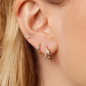 Close-up of elegant gold huggie hoops and stud earrings set with sparkling zircons