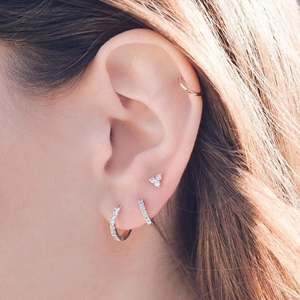 Close-up of 14K rose gold pavé huggie hoops and stud earrings on a model ear