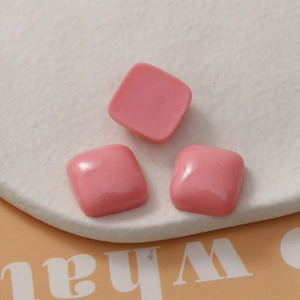 Close-up of three pink 15mm square resin cabochons on a white stone tray for DIY jewelry