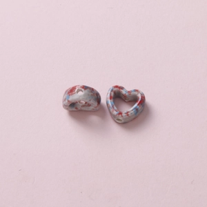 Macro detail of camouflage heart ceramic beads with red blue ink splash and side hole