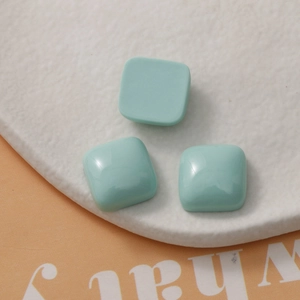 Macro detail of glossy light mint green square resin charms on a white stone tray
