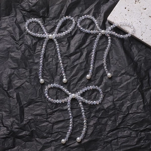 Close-up of three handmade iridescent beaded bow charms with white pearls on black texture