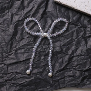 Macro detail of a crystal beaded bow with hanging faux pearls on a black textured background