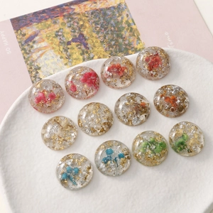 Macro shot of colorful dried flowers and gold foil inside round resin cabochons for DIY