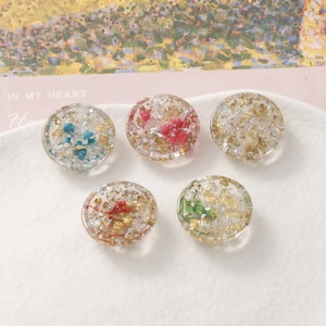 Detailed close-up of resin round charms with gold foil and dried flowers for DIY jewelry