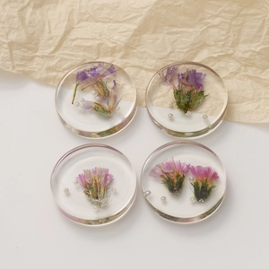 Macro shot of 4 clear resin round pendants with dried flowers and pearls for DIY jewelry