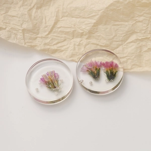 Detailed macro view of clear resin earrings with purple dried flowers and white pearls