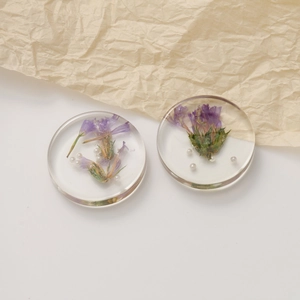 Macro detail of handmade resin earrings with embedded purple dried flowers and white pearls