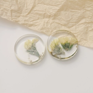 Macro detail of transparent resin earrings with dried yellow flowers and small white pearls