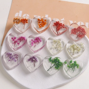 Macro shot of transparent heart resin charms with colorful dried flowers in a white tray