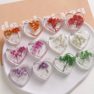Macro view of handmade heart resin charms with colorful dried flowers and pearls