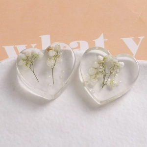 Macro detail of heart-shaped resin charms with white dried flowers and pearls inside