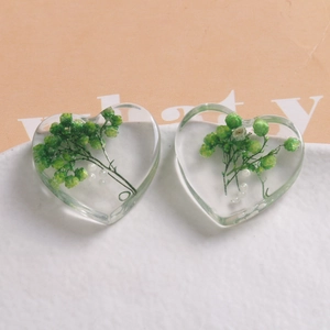 Macro shot of heart-shaped resin charms featuring real green dried flowers and white pearls