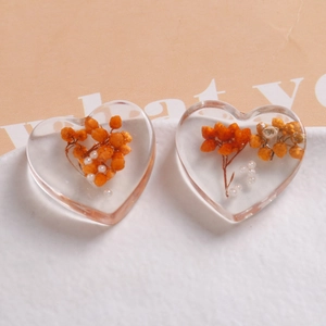 Macro view of transparent resin heart charms with orange dried flowers and white pearls