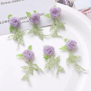 Handmade beaded wisteria flower earrings with purple and green beads on white plate