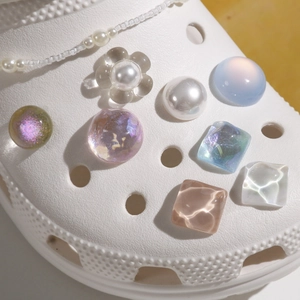 Detailed macro view of colorful aurora resin charms and pearl chain on white clog shoes