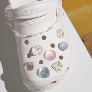Detailed view of iridescent crystal charms and a pearl chain on white garden clogs