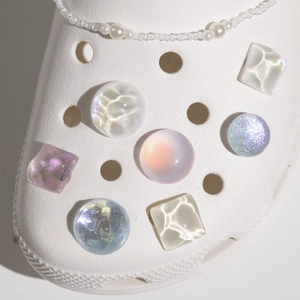 Close-up of iridescent crystal charms and pearl chain on a white garden clog shoe
