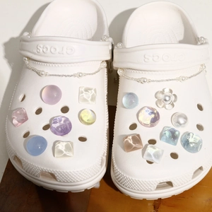 Macro detail of iridescent glitter charms and pearl chains on white clog shoes