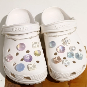 Detail of white clogs featuring colorful glitter charms and elegant pearl chains