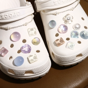 Close-up of glitter water-wave gems and pearl chain DIY charms on white clogs