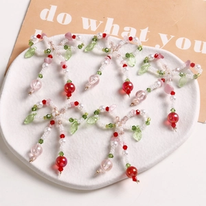 Close-up of handmade beaded bow charms with green leaves and red berry beads in a dish